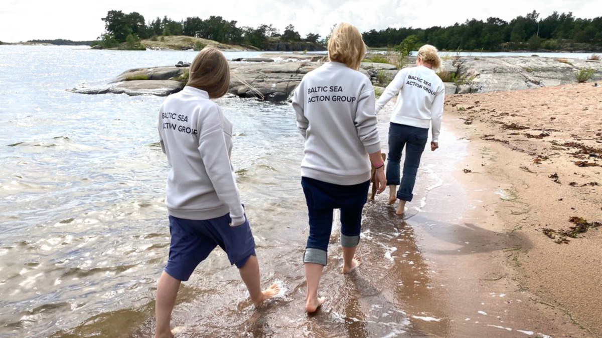 Pieta, Laura ja Michaela kävelevät Itämeren rannalla Baltic Sea Action Groupin collage-paidat päällä.