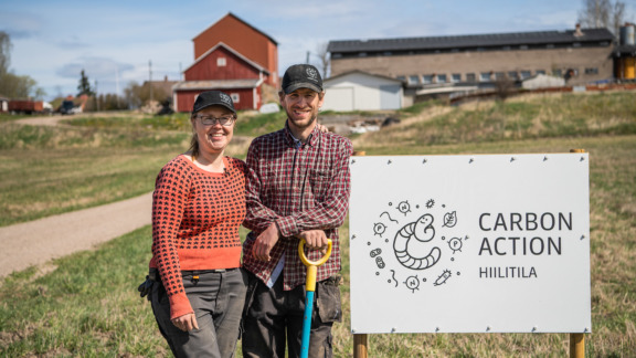 Viljelijäpari Patrik Nyström ja Sirkku Puumala seisovat Carbon Action Hiililtila -kyltin vieressä.