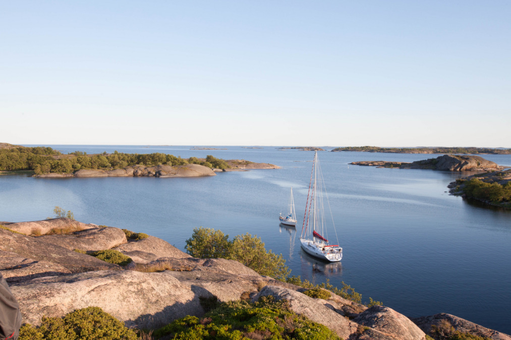 Purjeveneitä kallioisen rannan lähistöllä. Taustalla sininen, pilvetön taivas.