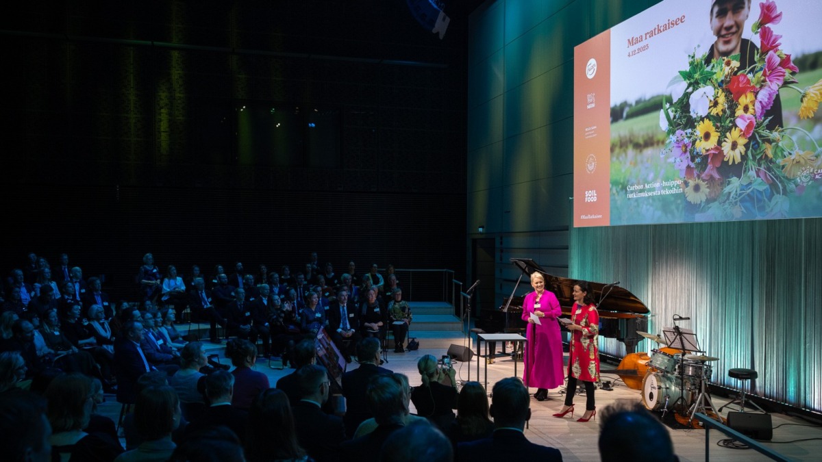 Suuressa salissa ihmisiä istumassa. Lavalla kaksi naista juontaa Maa ratkaisee -tapahtumaa. Musiikkitalon Paavo-sali, Helsinki.