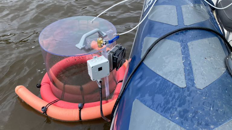 Pyöreä mittalaite kumiveneen vieressä veden pinnalla kellukkeiden päällä.